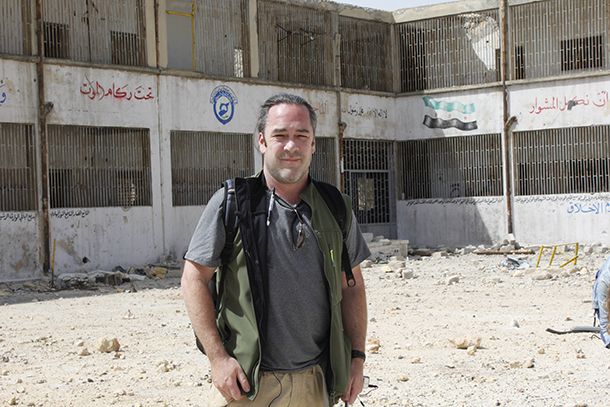 Reporter Patrick Henningsen in the courtyard of the White Helmets training center in Hanano, East Aleppo in May 2017. Behind him, you can clearly see the Free Syrian Army flag and the White Helmets brand displayed together.