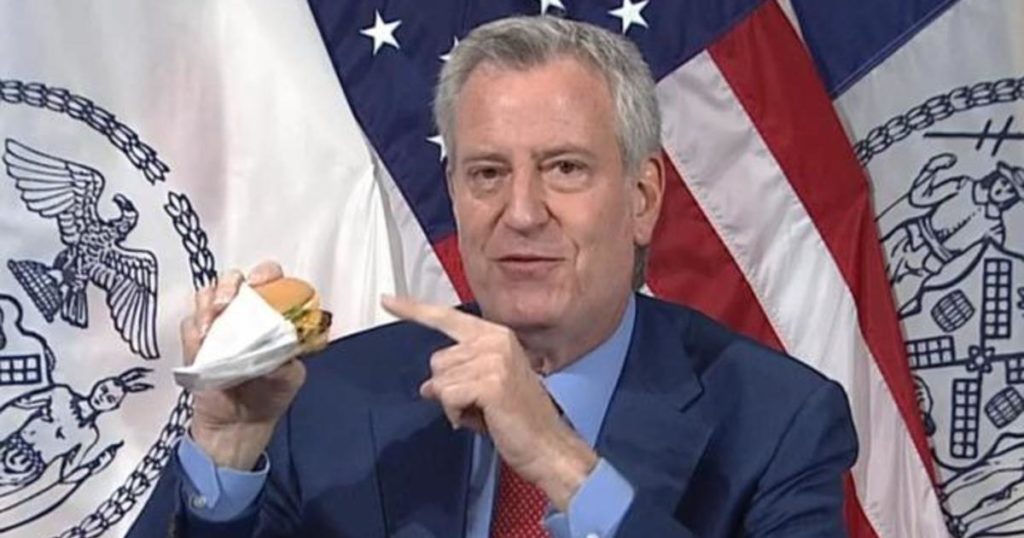 Mayor Bill de Blasio points to a hamburger.